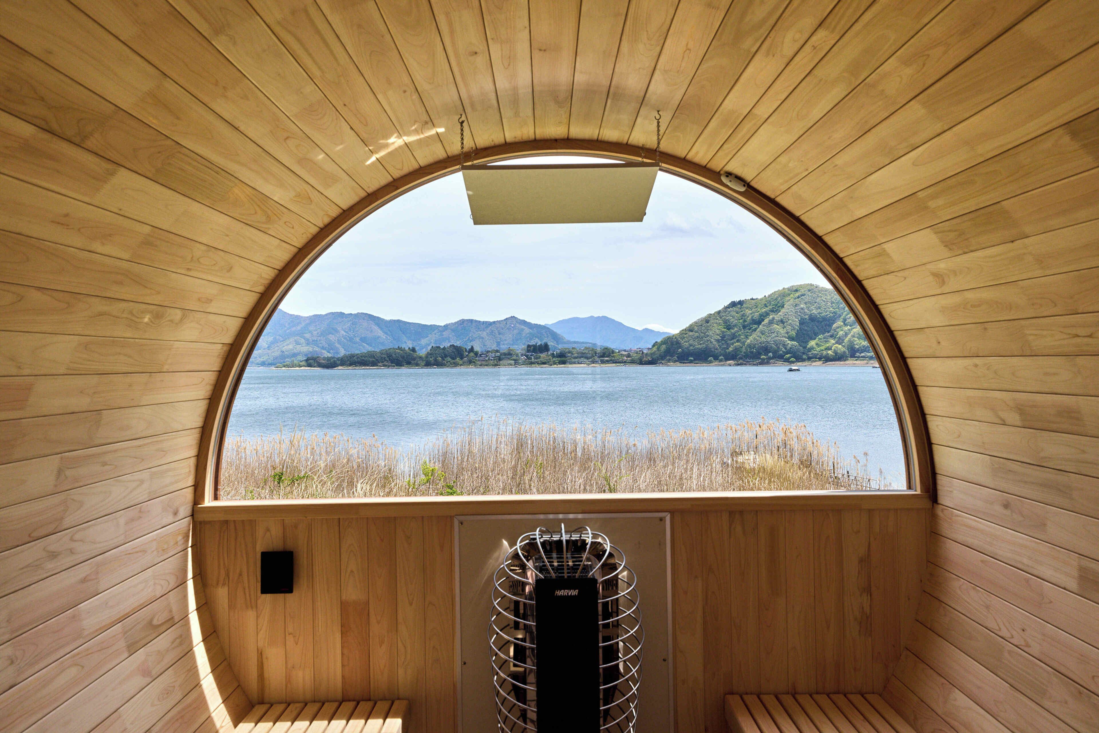 Una baita di legno con un'ampia finestra ad arco che si affaccia su un lago e delle montagne.