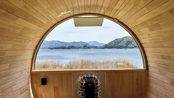 Una baita di legno con un'ampia finestra ad arco che si affaccia su un lago e delle montagne.