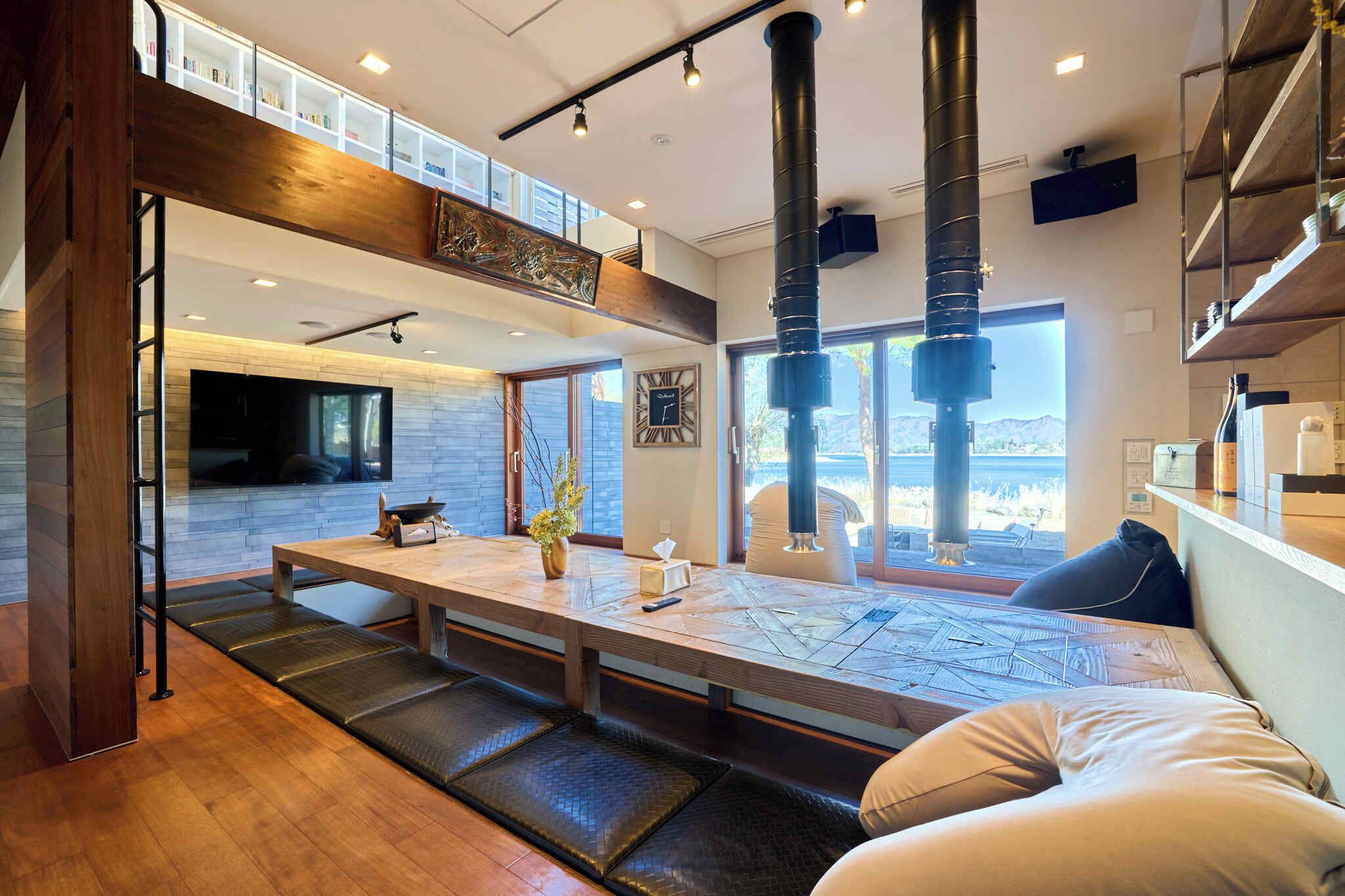A modern interior with a long dining table, seating, and a view through large windows.