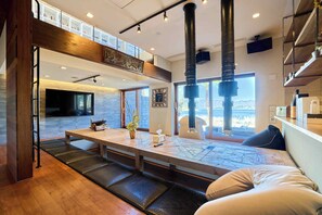A modern interior with a long dining table, seating, and a view through large windows.