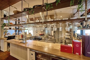 Una cocina moderna con encimera de madera, electrodomésticos de acero inoxidable, copas de vino colgantes y plantas en macetas.