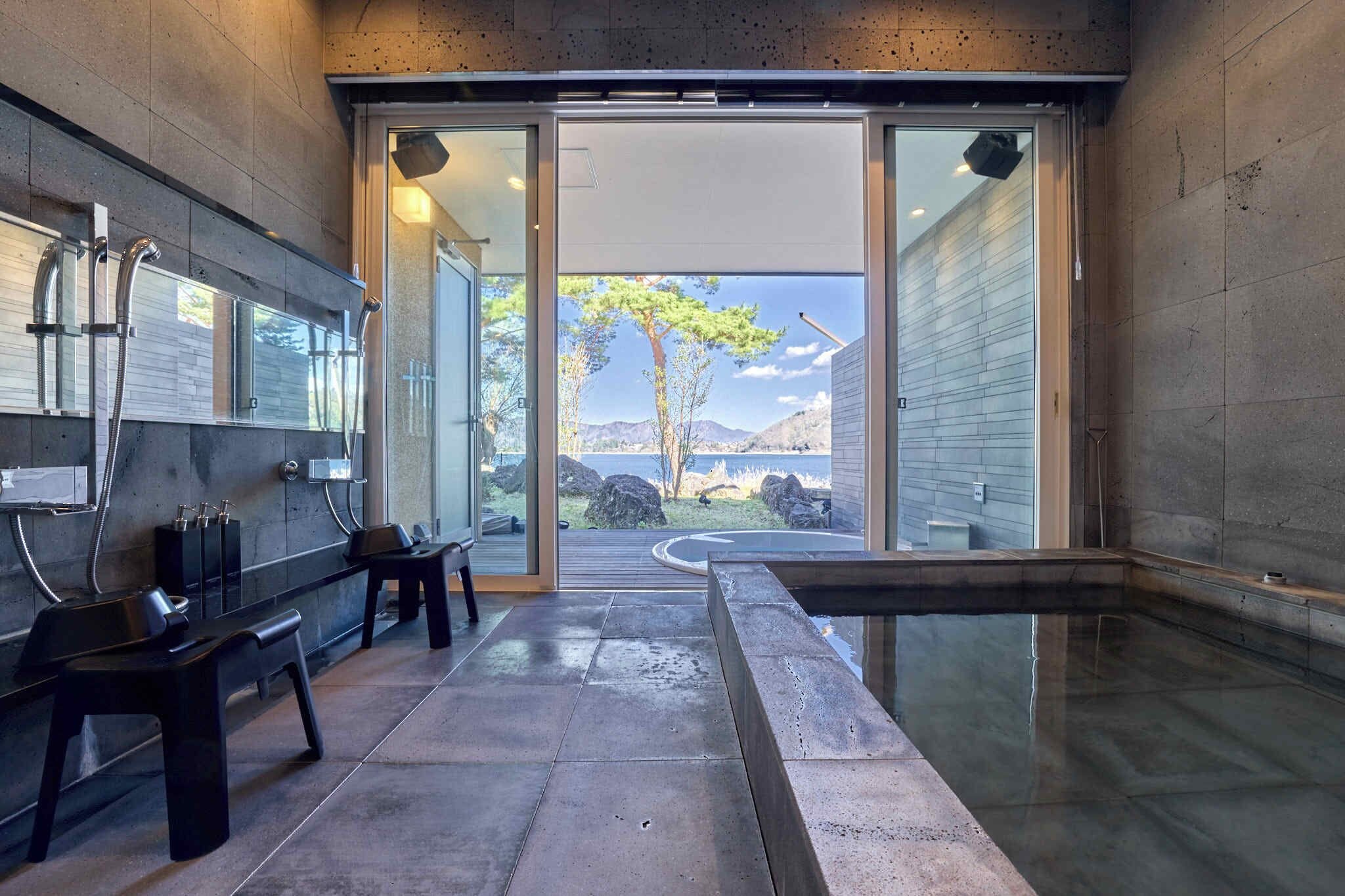 A modern bathroom with a glass shower enclosure, a bench, and a view of a tree and mountains.