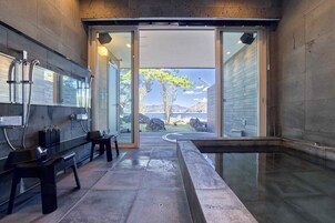 A modern bathroom with a glass shower enclosure, a bench, and a view of a tree and mountains.