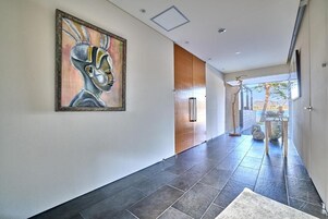 Un pasillo moderno con un cuadro abstracto grande, una puerta de madera y vistas al exterior.