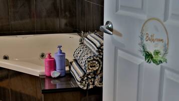 A bathroom with a bathtub, a towel rack with rolled towels, and toiletries on the counter.