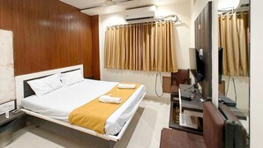 Habitación de hotel con cama, escritorio, televisión, aire acondicionado y espejo.