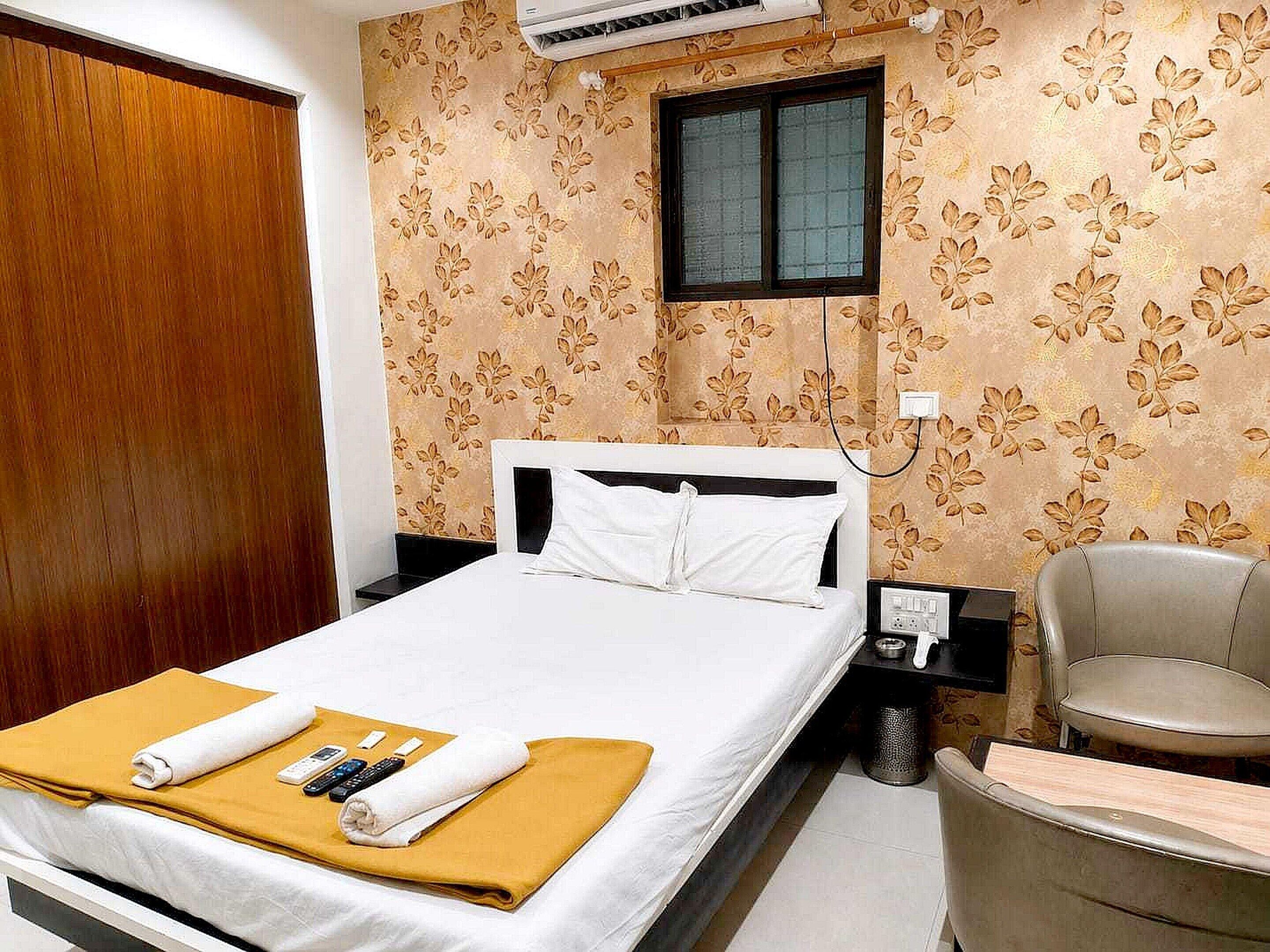 A hotel room with a bed, a chair, a nightstand, and a window.