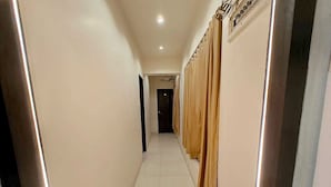 Un pasillo con suelo de baldosas, una puerta al final y cortinas en la pared derecha.
