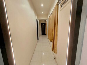 A corridor with a tiled floor, a door at the end, and curtains on the right wall.