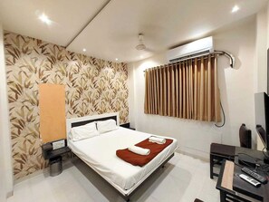 Habitación de hotel con cama, escritorio con silla, unidad de aire acondicionado y televisor montado en la pared.