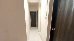 Un pasillo estrecho con una puerta oscura al final, paredes blancas y un interruptor de luz en la pared.
