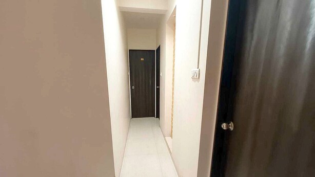 Un pasillo estrecho con una puerta oscura al final, paredes blancas y un interruptor de luz en la pared.