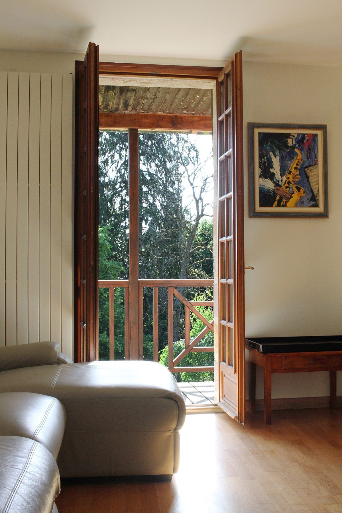 Una habitación con puerta de vidrio corredera que da a un balcón, un sofá, una mesita y un cuadro en la pared.