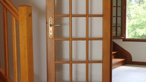 Une porte en bois ornée d’un motif quadrillé, un escalier en bois et un sol carrelé.