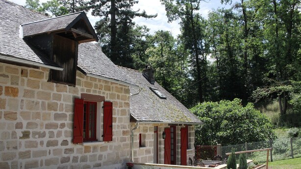 Un bâtiment en pierre avec des volets rouges, un petit porche et une allée gravillonnée.