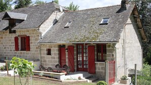 Une maison en pierre avec des volets rouges, un toit en pente et un petit jardin.
