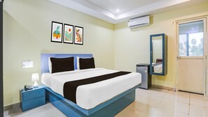 A hotel room with a bed, a nightstand, a desk, an air conditioner, a mirror, and framed artwork on the wall. - Classic With Twin Bed Hotel Rama Royal (Nellore)