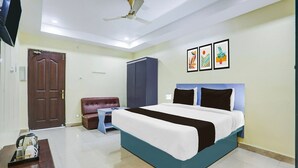 A hotel room with a bed, a desk, a chair, a wardrobe, and a ceiling fan. - Classic With Twin Bed Hotel Rama Royal (Nellore)