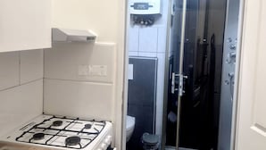 A compact kitchen with a gas stove, a sink, and a small oven. There is a glass-enclosed shower area with a toilet visible in the background. - 10 Min to Westbahnhof 1BR with Living (Wien)
