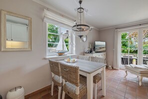 A dining area with wicker chairs, a white table, a chandelier, and a view of the outdoors through a window. - Wencke - Westerland (Westerland)
