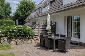 Une terrasse avec une table et des chaises, un mur en pierre et un bâtiment doté d’un toit en tuiles et de grandes fenêtres.