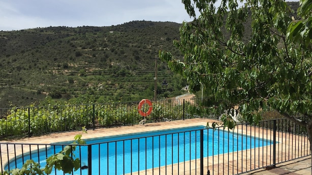 A swimming pool with a black metal fence, surrounded by greenery and hills in the background. - Rural Cottage for a Romantic Retreat (Laroya)