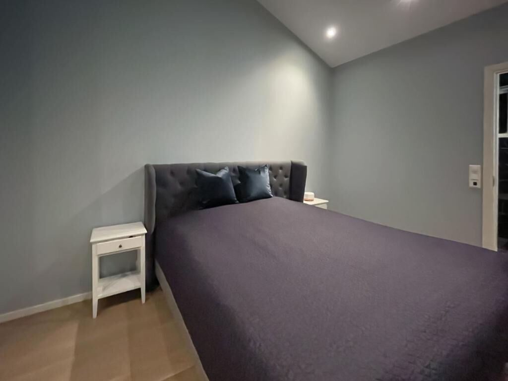 Un dormitorio con cama, mesita de noche y toma de corriente.