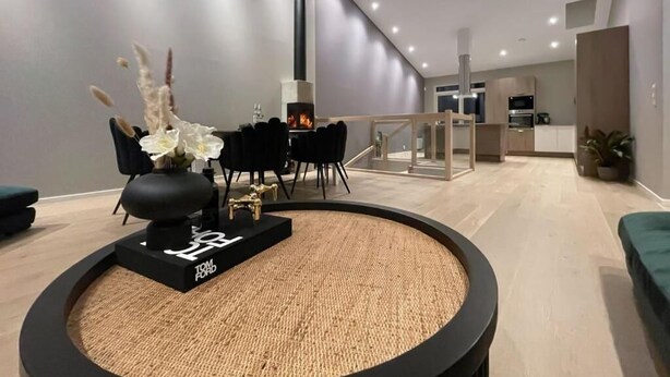 Una sala moderna con una mesa de centro redonda tejida, una chimenea y un comedor al fondo.