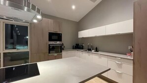 Una cocina moderna con una isla central, horno empotrado y muebles blancos.