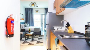 A modern kitchen with a refrigerator, stove, and sink. There is a fire extinguisher mounted on the wall. - Bloomfields Studio In Oasis 1 - Masdar (Masdar)