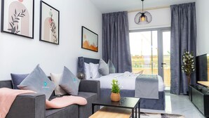 A modern bedroom with a bed, grey sofa, and a small table. - Bloomfields Studio In Oasis 1 - Masdar (Masdar)