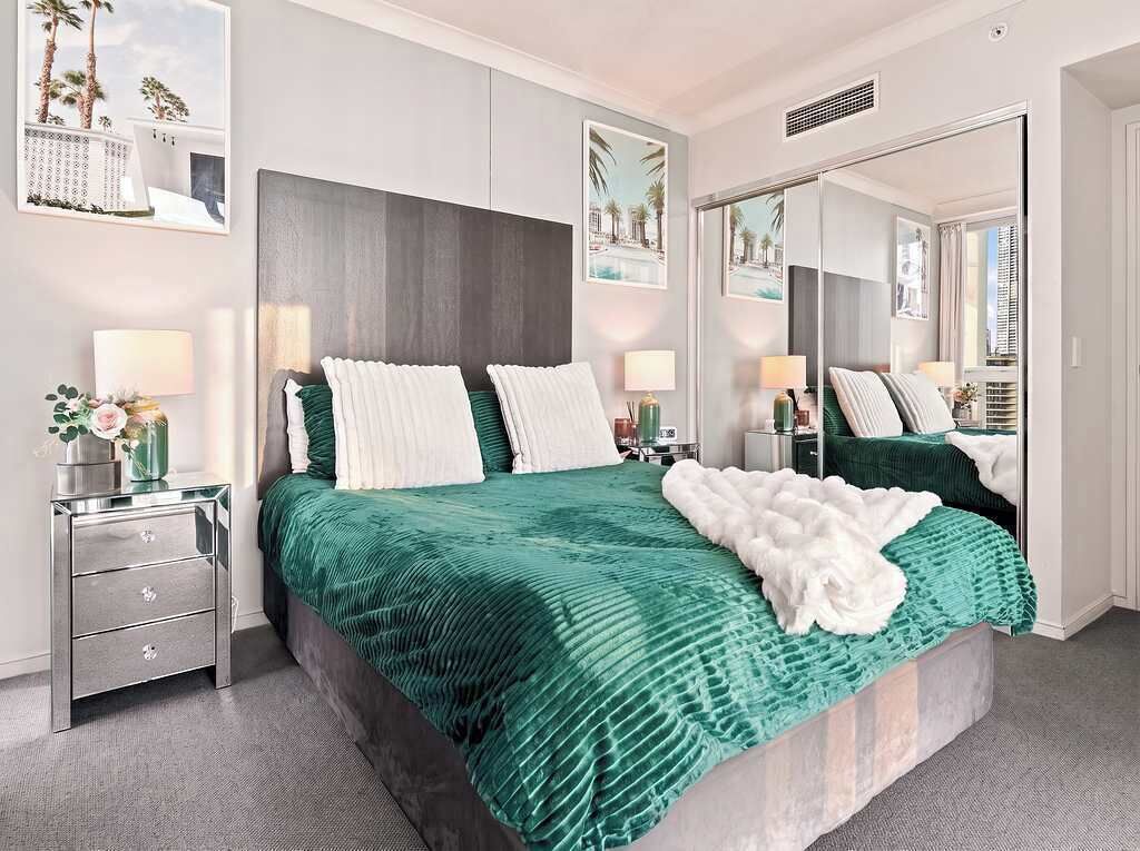Ein Hotelzimmer mit einem großen Bett, zwei Nachttischen, einem Spiegel und Bildern an den Wänden.