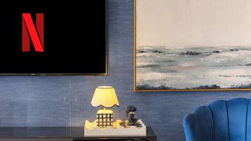 A modern living room with a flat-screen TV, a blue armchair, a lamp, a sculpture, and a painting on the wall.