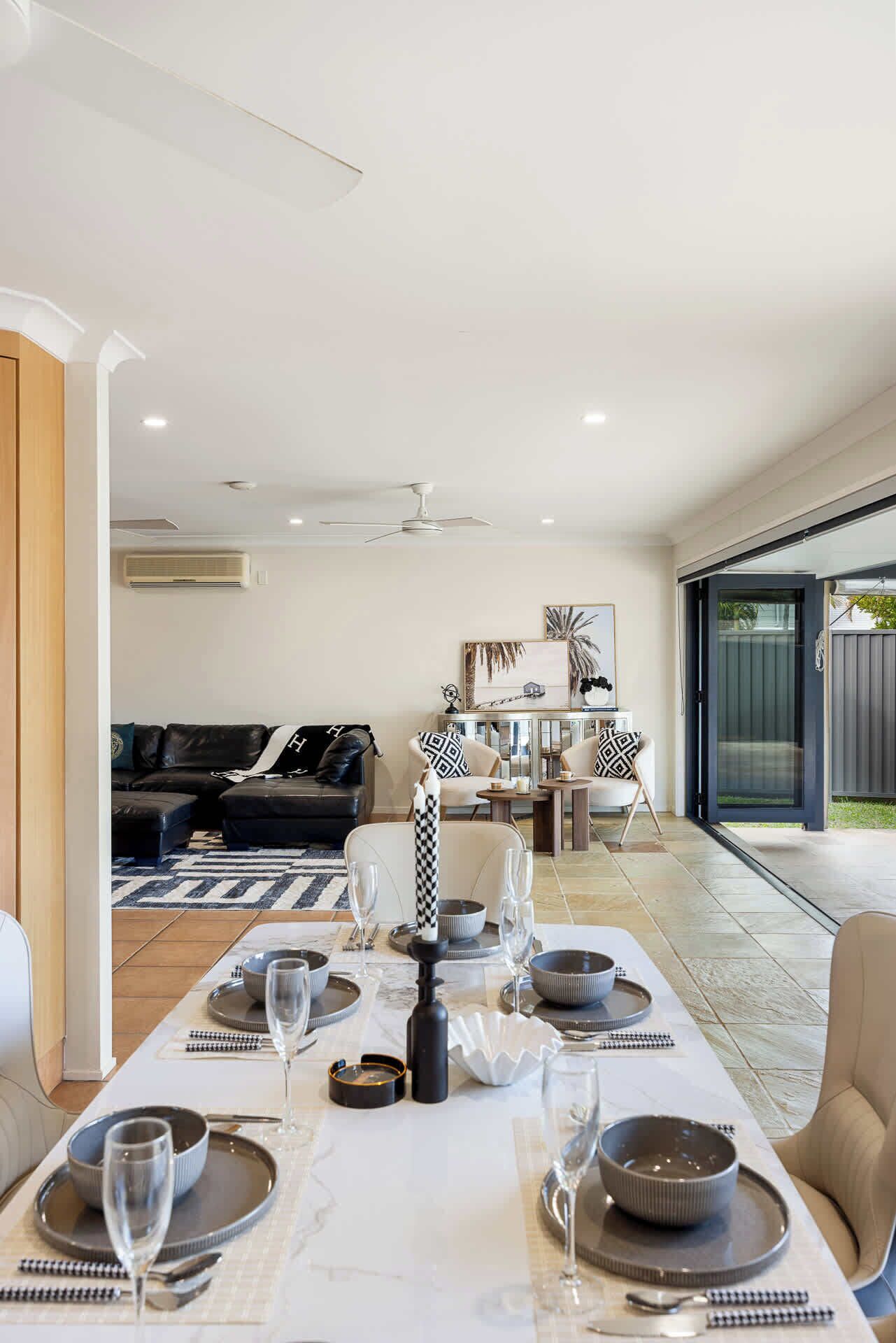 A modern dining area with a long table set for six, a sofa, and a dining table with a view to the outside.