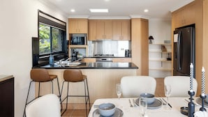 Eine moderne Küche mit Holzausstattung, einem Edelstahlkühlschrank und einem Essbereich mit weißen Stühlen und einem Tisch für zwei Personen.