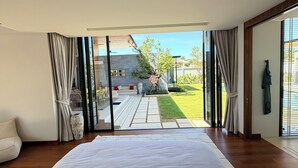 A bedroom with a large bed, a view of the garden, and a sliding glass door leading outside. - BRAND-NEW LUXURY VILLA IN THE BOTANICA FORESTIQUE RESIDENCE IN PHUKET, NEAR THE GOLF COURSE (Choeng Thale)