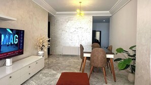 Una sala de estar moderna con televisor de pantalla plana, comedor con sillas, una mesa de centro de mármol y una lámpara en el techo.