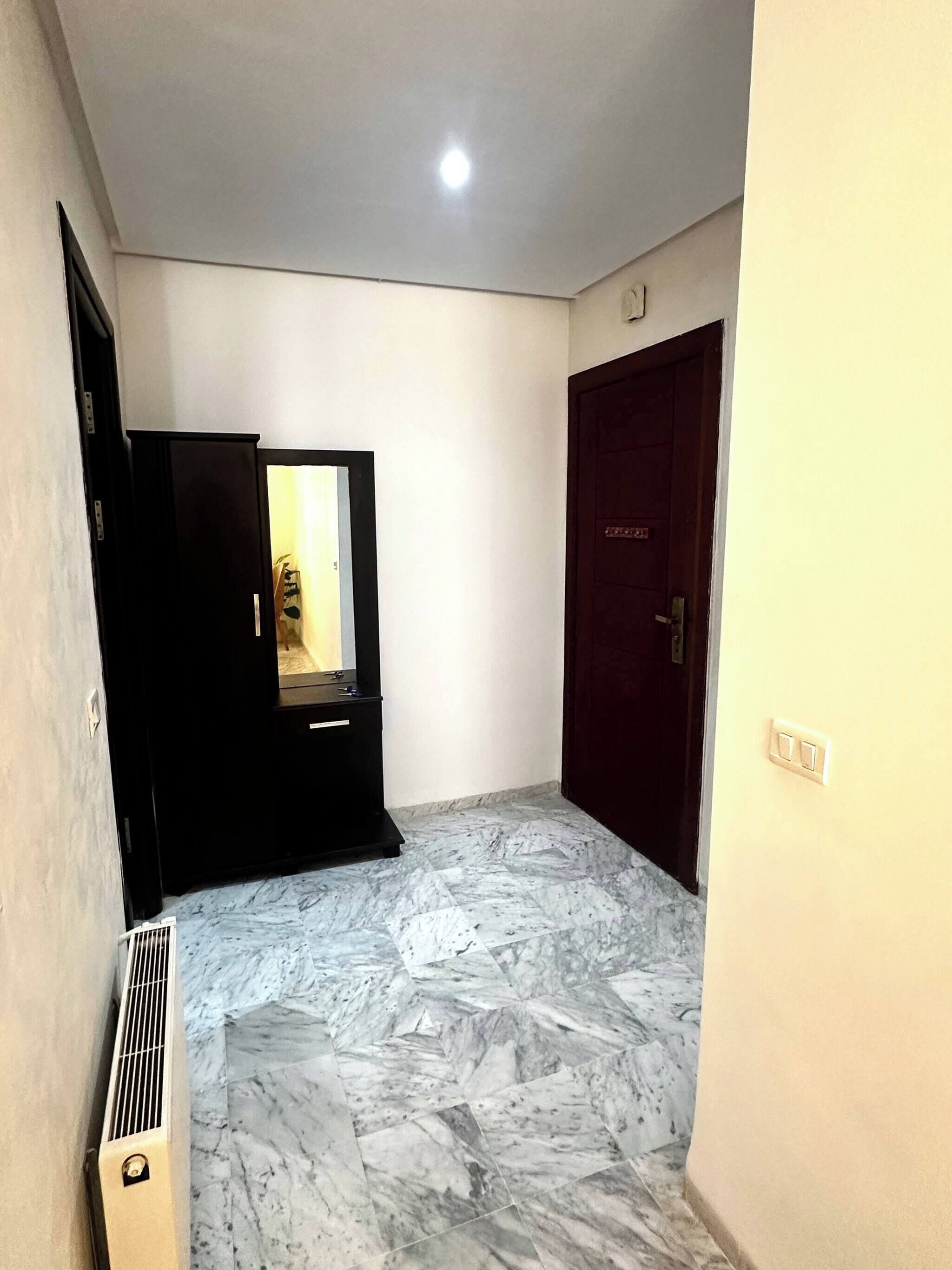 A room with a marble floor, a closed door, a dark-colored wardrobe, and a vent on the wall.