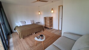 Ein Schlafzimmer mit einem Bett, einem Holzschrank, einem runden Tisch mit einer Zeitschrift, einer Couch und zwei Pendelleuchten.