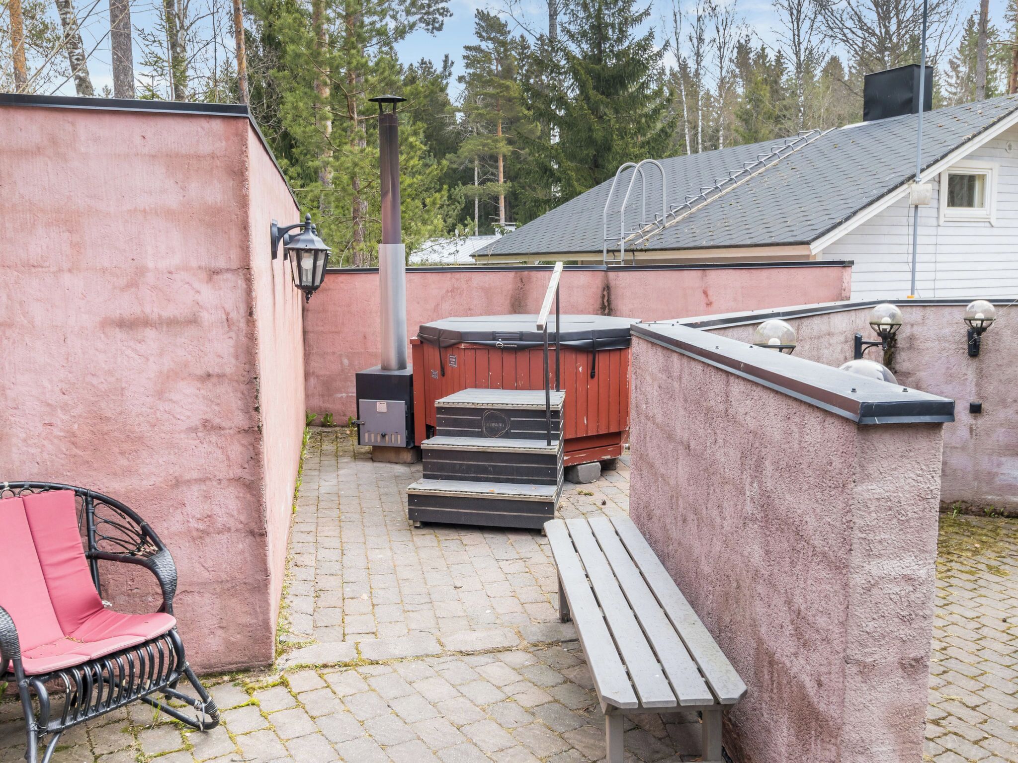 Un espace extérieur aménagé avec un banc en bois, une chaise rouge, un jacuzzi et un sauna.