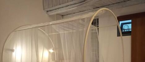 A single bed with a canopy, a small window, and a wooden ceiling.