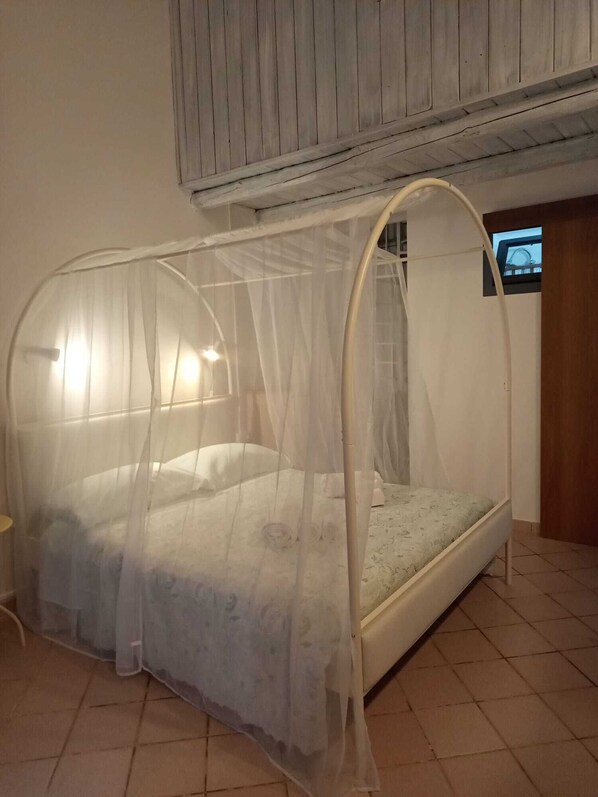 A single bed with a canopy, a small window, and a wooden ceiling.