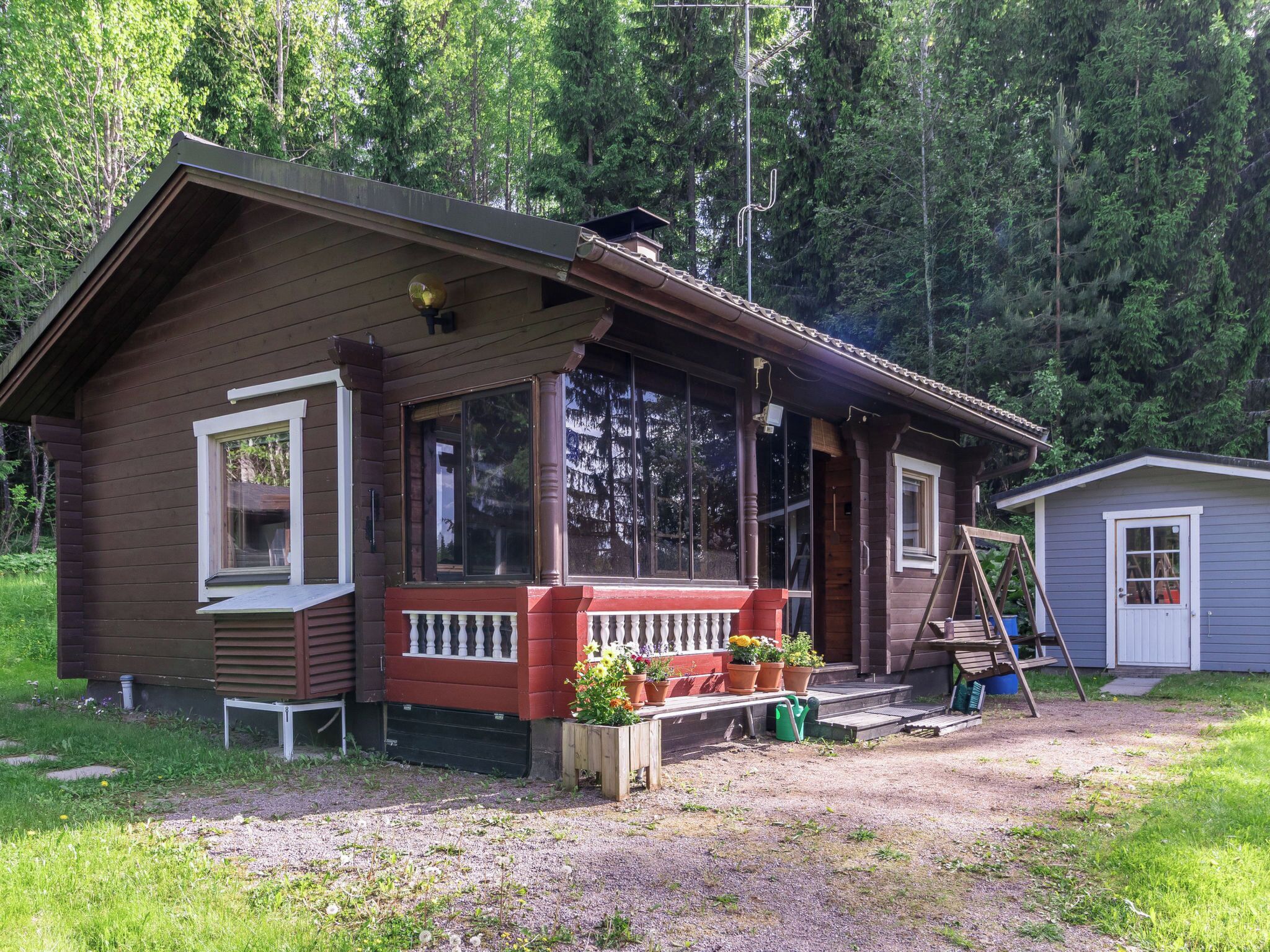 A wooden cabin with a porch, a small shed, and a ladder.