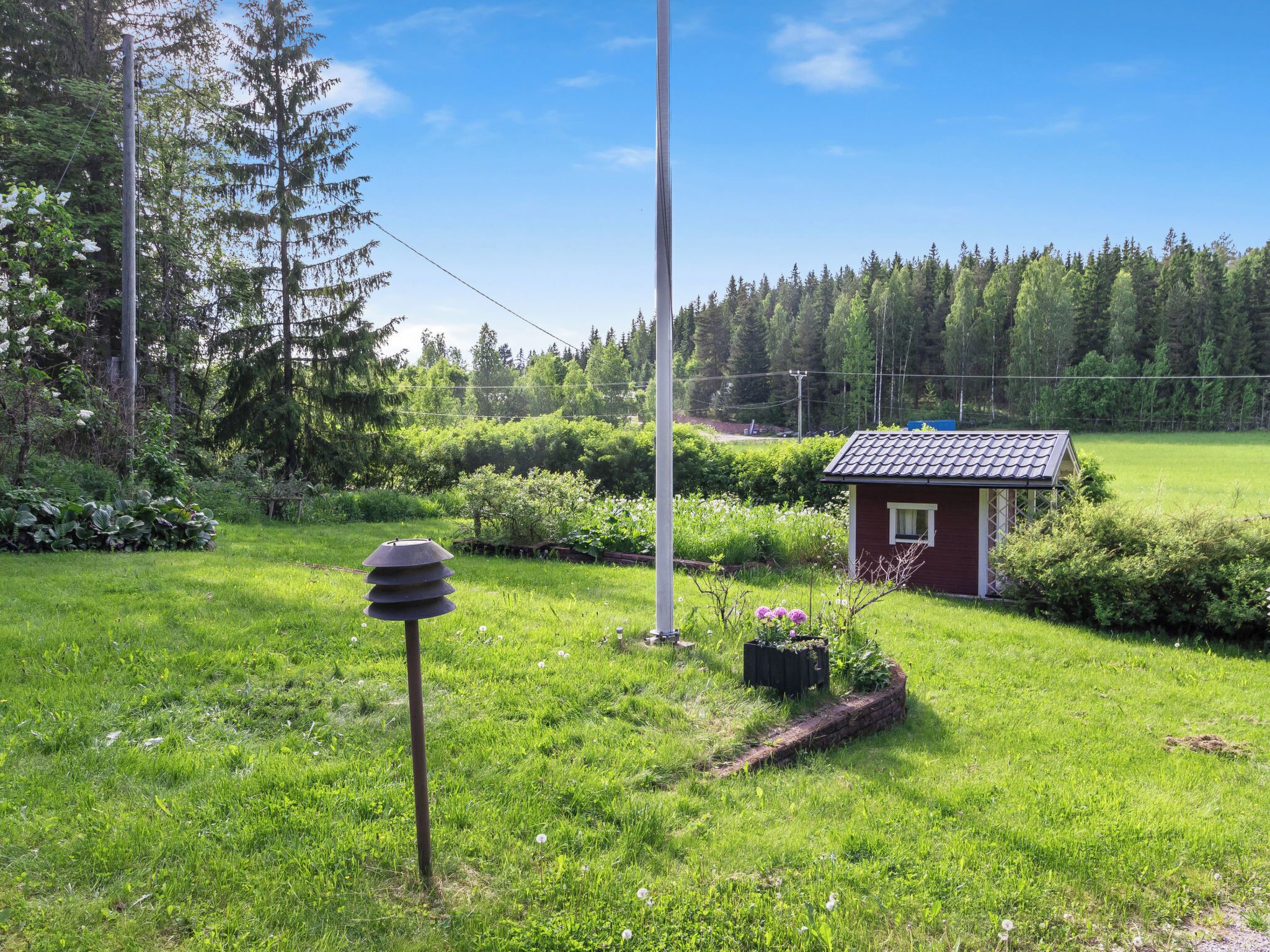 Ett litet rött hus med ett tak täckt av tegelpannor, omgivet av frodigt grönt gräs och träd.
