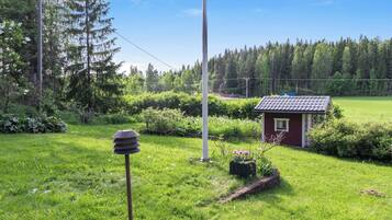 Ett litet rött hus med ett tak täckt av tegelpannor, omgivet av frodigt grönt gräs och träd.