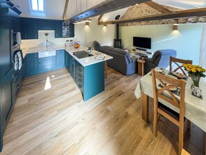 A modern kitchen with a central island, a dining area with a table and chairs, and a cozy seating area with a sofa and a TV. - All on the Ground Floor: 
Open plan living space. (Yarcombe)