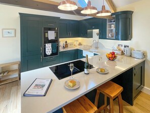 A modern kitchen with dark teal cabinets, a white countertop, and a central island with a bottle of wine and a glass. - All on the Ground Floor: 
Open plan living space. (Yarcombe)