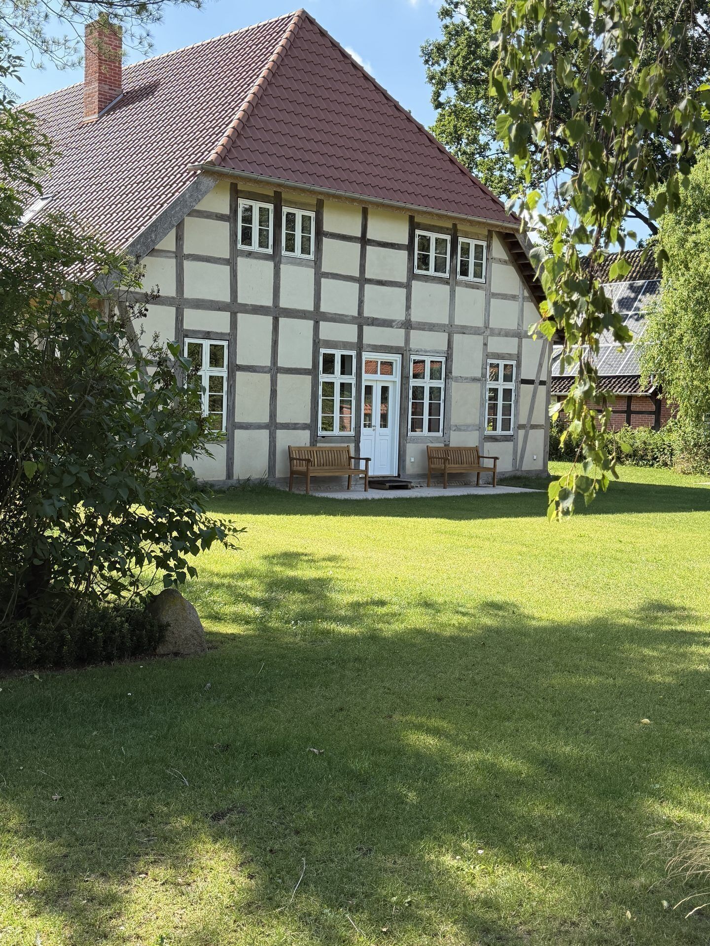 A traditional half-timbered house with a red-tiled roof, two wooden benches, and a white door.
