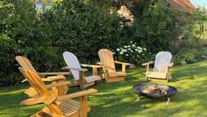 Adirondack stoelen rond een vuurkuil op een gazon.