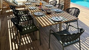 Ein Essbereich im Freien mit Blick auf einen Pool, einer Holzterrasse und schwarzen Stühlen.